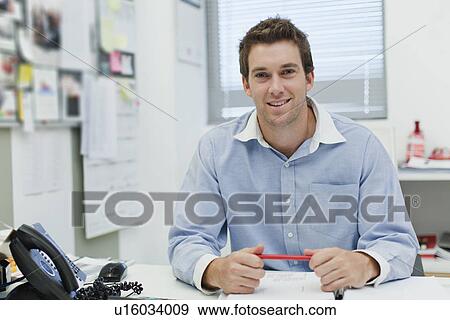 Smiling businessman sitting at desk View Large Photo Image Stock Photo - Smiling businessman sitting at desk. Fotosearch