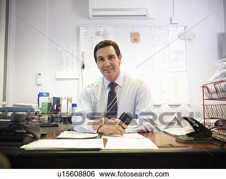 Stock Photograph - Smiling businessman sitting at desk. Fotosearch