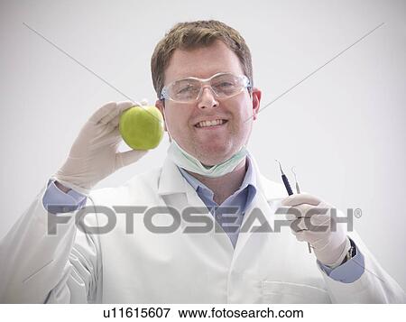 Smiling dentist holding apple View Large Photo Image Stock Photo - Smiling dentist holding apple. Fotosearch