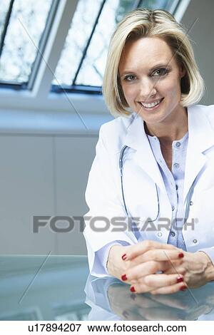 Stock Photo - Smiling doctor sitting at desk. Fotosearch