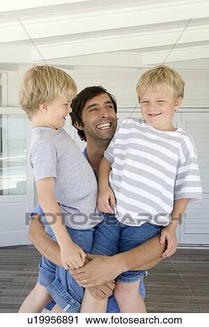 Stock Image - Smiling father holding sons. Fotosearch