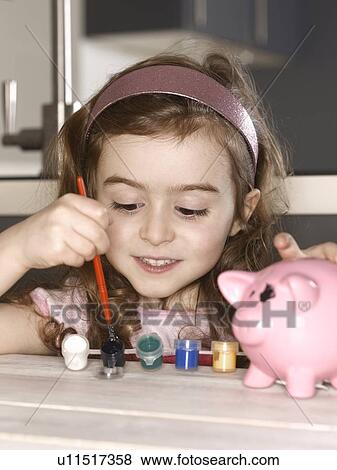 Stock Photo - Smiling girl painting piggy bank. Fotosearch