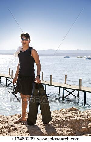 Stock Photo - Snorkeler carrying fins on sandy beach. Fotosearch