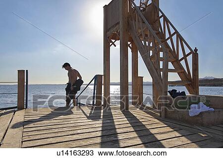 Stock Image - Snorkeler putting on wetsuit by water. Fotosearch