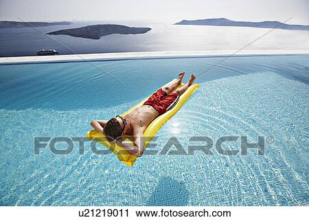 Stock Image - Teenage boy relaxing on raft in pool. Fotosearch