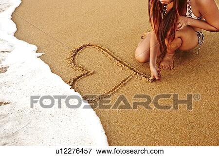 Stock Photo - Teenage girl drawing heart in sand. Fotosearch
