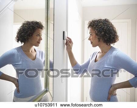 Stock Image - Woman adjusting thermostat in home. Fotosearch