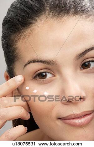 Stock Image - Woman applying moisturizer to face. Fotosearch