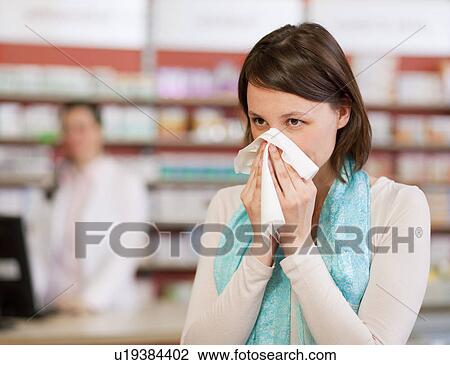 Stock Image - Woman blowing nose in pharmacy. Fotosearch