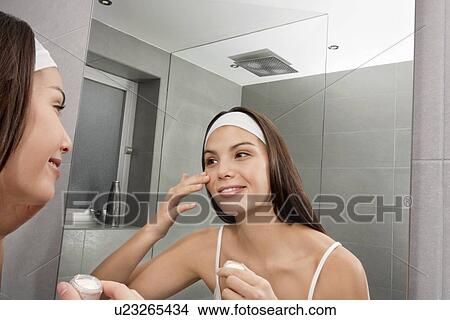 Picture - Woman examining her face in mirror. Fotosearch
