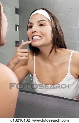 Stock Image - Woman examining her teeth in mirror. Fotosearch