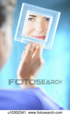 Stock Image - Woman examining herself in mirror. Fotosearch