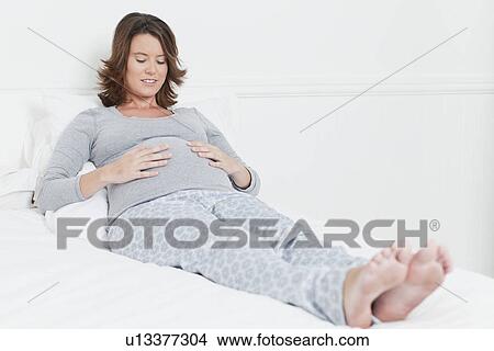 Woman holding pregnant belly on bed View Large Photo Image Picture - Woman holding pregnant belly on bed. Fotosearch