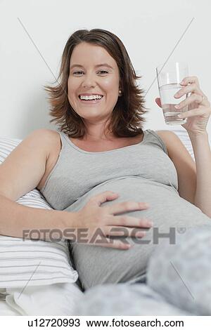 Stock Image - Woman holding pregnant belly on bed. Fotosearch
