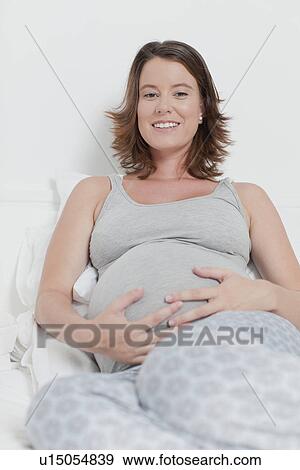 Stock Photo - Woman holding pregnant belly on bed. Fotosearch