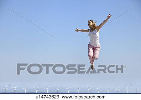Woman jumping for joy over wind turbines View Large Photo Image Stock Photo - Woman jumping for joy over wind turbines. Fotosearch