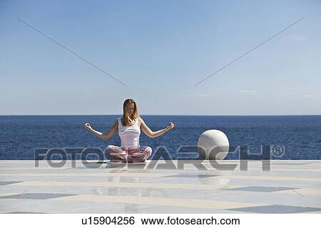 Stock Photograph - Woman meditating on tiled surface. Fotosearch