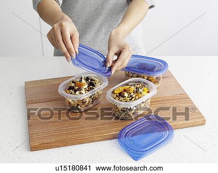 Stock Image - Woman packing granola in tupperware. Fotosearch