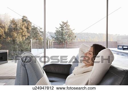 Stock Image - Woman relaxing on sofa in living room. Fotosearch