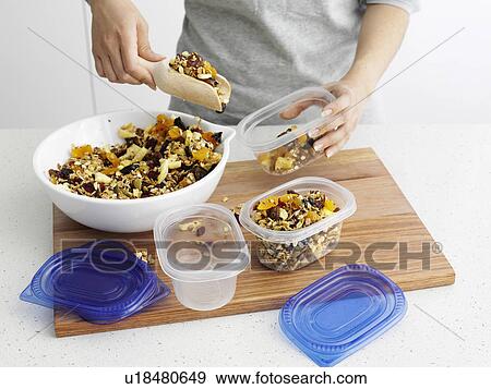 Stock Photo - Woman scooping granola into tupperware. Fotosearch