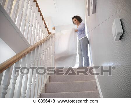 Stock Photo - Woman shaking out sheets on staircase. Fotosearch
