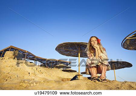 Stock Photo - Woman sitting on beach cliffs. Fotosearch