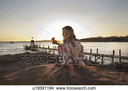 Picture - Woman sitting on rocky beach. Fotosearch