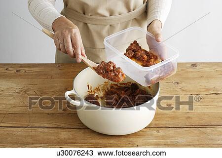 Stock Image - Woman spooning meat into tupperware. Fotosearch