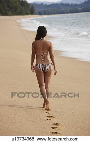 Stock Photo - Woman walking on sandy beach. Fotosearch