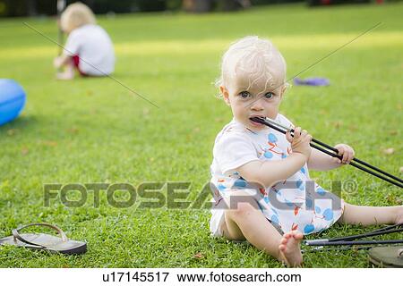 Stock Photo - Baby girl chewing on toys in backyard. Fotosearch