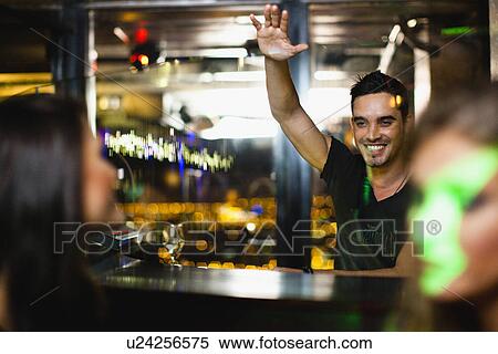Stock Photography - Bartender waving to customers in bar. Fotosearch