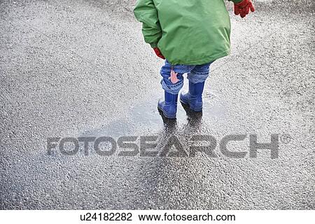 Stock Image - Boy in rain boots playing in puddle. Fotosearch