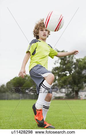 Stock Photo - Boy playing with soccer ball in field. Fotosearch