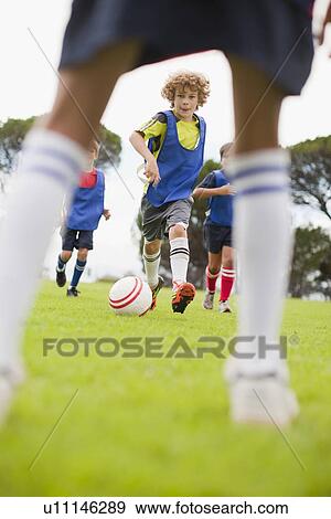 Stock Photo - Boys playing soccer on pitch. Fotosearch