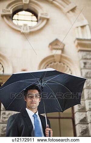 Stock Image - Businessman carrying umbrella on street. Fotosearch