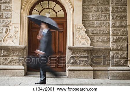 Businessman carrying umbrella on street View Large Photo Image Stock Image - Businessman carrying umbrella on street. Fotosearch