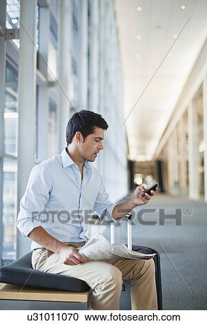 Stock Image - Businessman using cell phone in lobby. Fotosearch