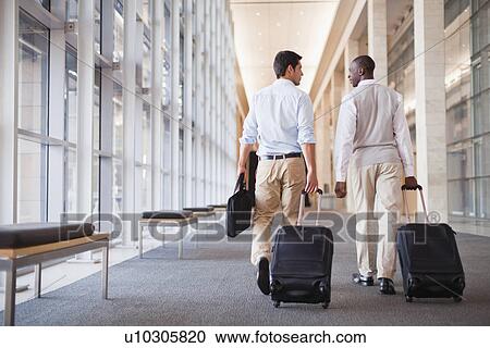 Stock Image - Businessmen rolling luggage in hallway. Fotosearch