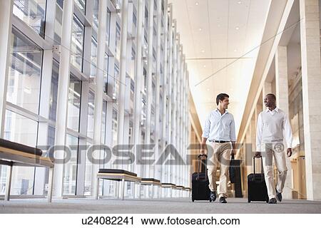 Stock Image - Businessmen rolling luggage in hallway. Fotosearch