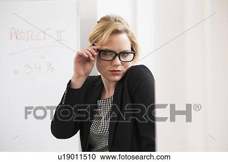 Stock Image - Businesswoman holding glasses in office. Fotosearch