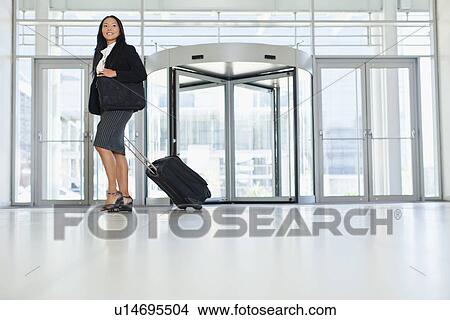 Businesswoman rolling luggage in lobby View Large Photo Image Picture - Businesswoman rolling luggage in lobby. Fotosearch