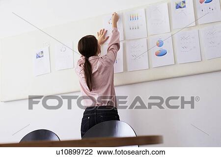 Stock Image - Businesswoman tacking up sign in office. Fotosearch