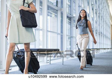 Businesswomen rolling luggage in hallway View Large Photo Image Stock Photo - Businesswomen rolling luggage in hallway. Fotosearch