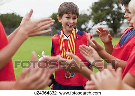 Stock Image - Children cheering teammate with trophy. Fotosearch