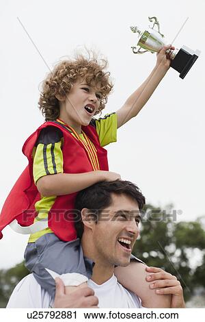 Stock Image - Coach carrying child with trophy. Fotosearch