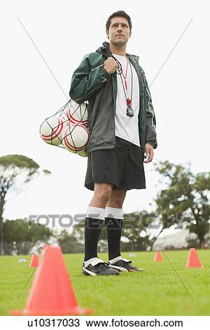 Stock Image - Coach carrying soccer balls on pitch. Fotosearch