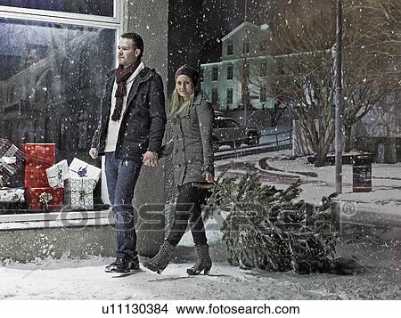 Picture - Couple carrying Christmas tree in snow. Fotosearch