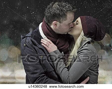 Stock Photo - Couple kissing in snow at night. Fotosearch
