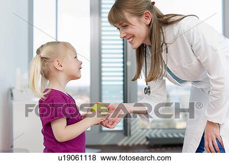 Doctor handing girl an apple in office View Large Photo Image Stock Photo - Doctor handing girl an apple in office. Fotosearch