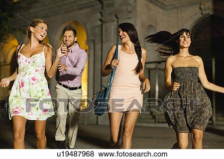 Friends walking on city street at night View Large Photo Image Stock Photo - Friends walking on city street at night. Fotosearch